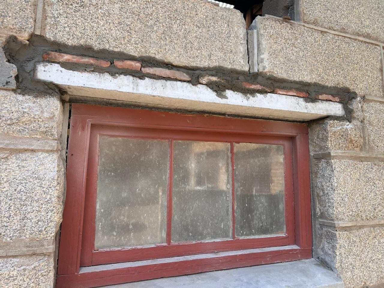 Restored red-framed window in stone wall